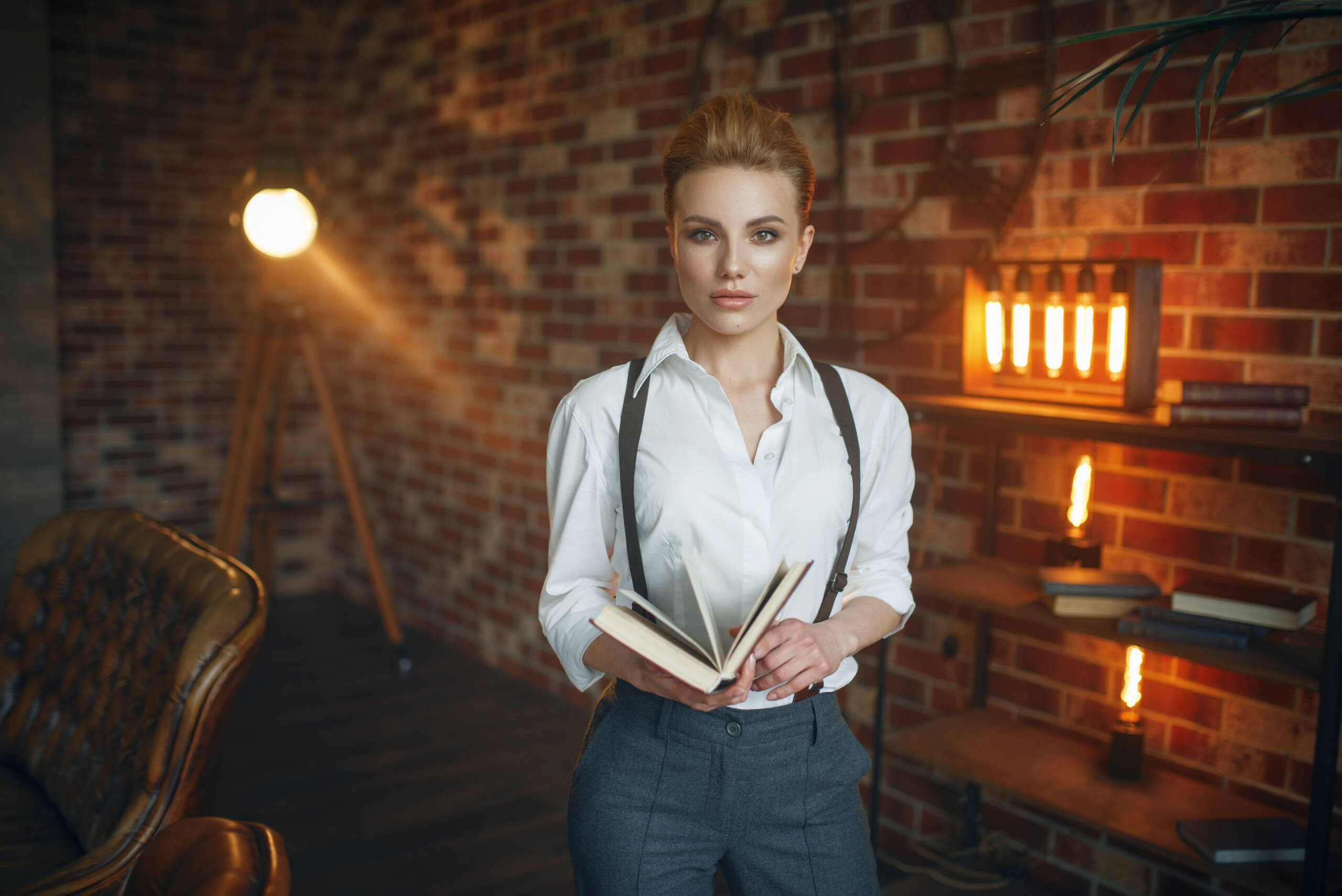 Business woman in strict clothes poses with book in studio, retro fashion, gangster style. Vintage lady in office with brick walls