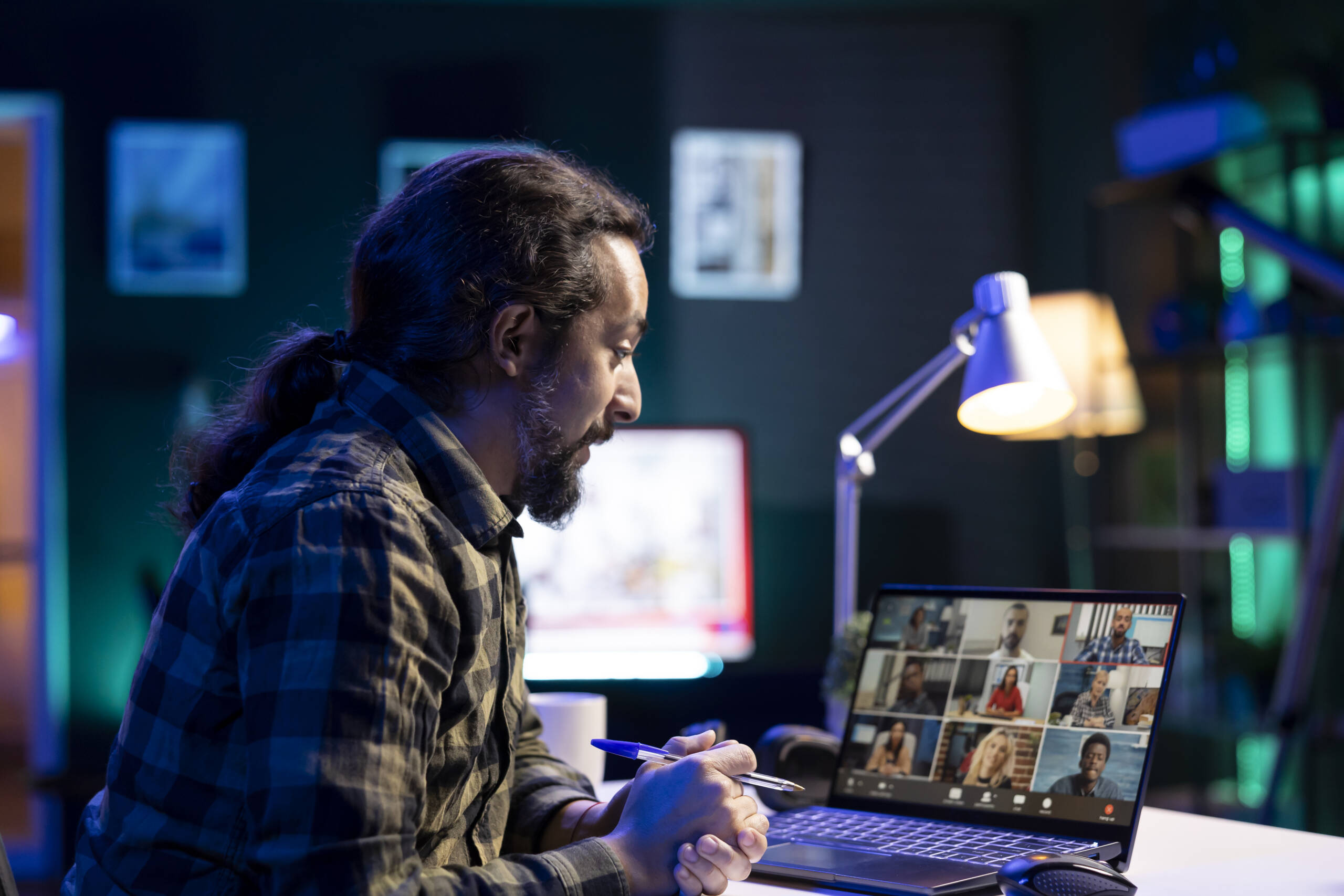 A man with a beard is comparing documents with a group of people from different backgrounds in a virtual meeting. Male person attending video conference on his digital laptop.
